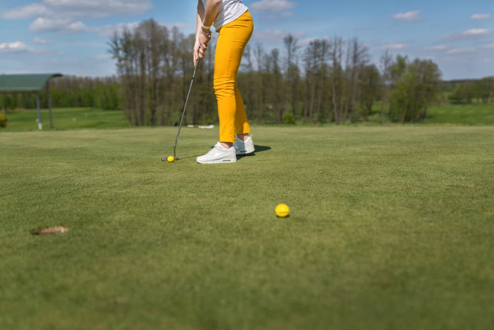 Woman in yellow pants plays golf.