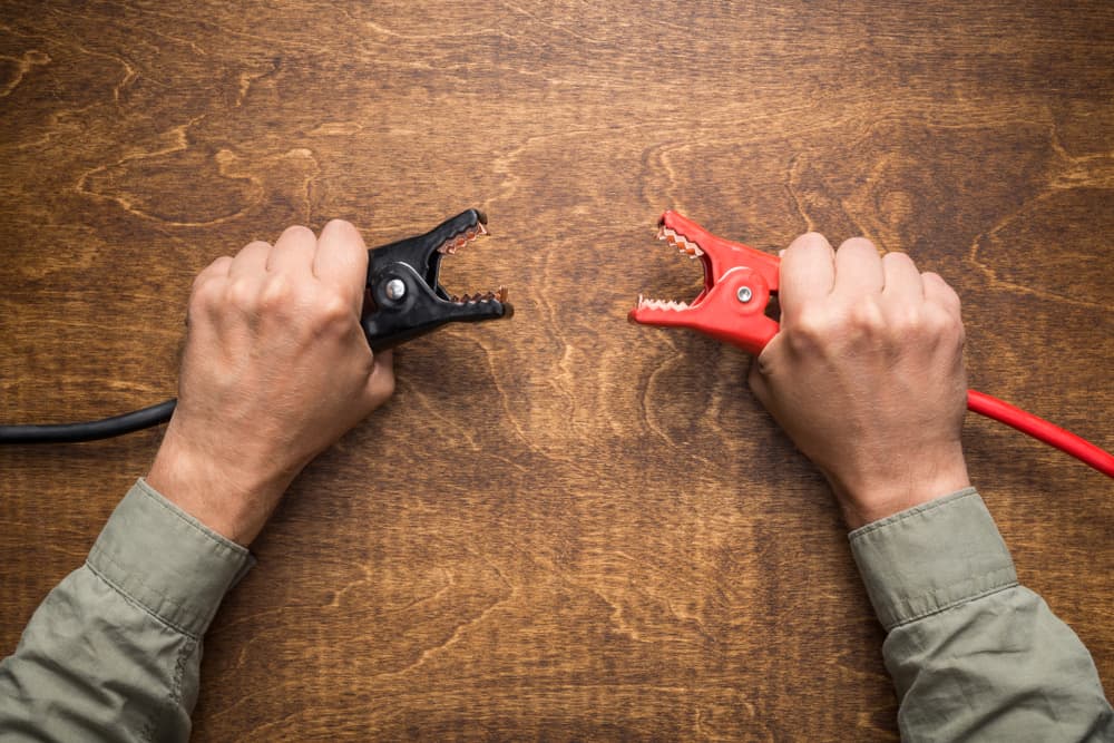 Hands holding car battery charging clamps