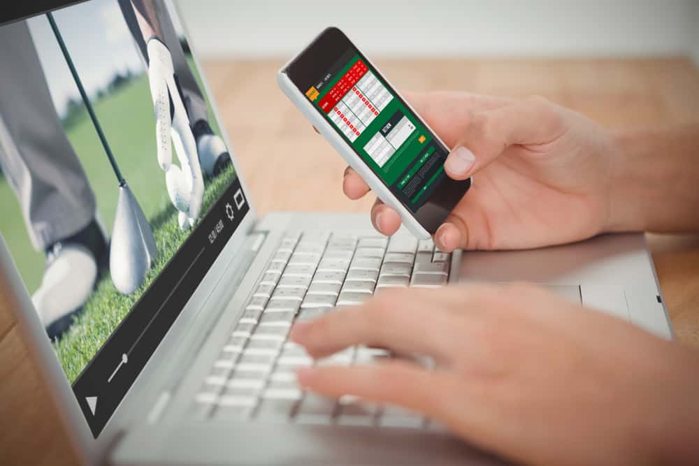 View of lecture app against man holding mobile phone while typing on laptop at desk