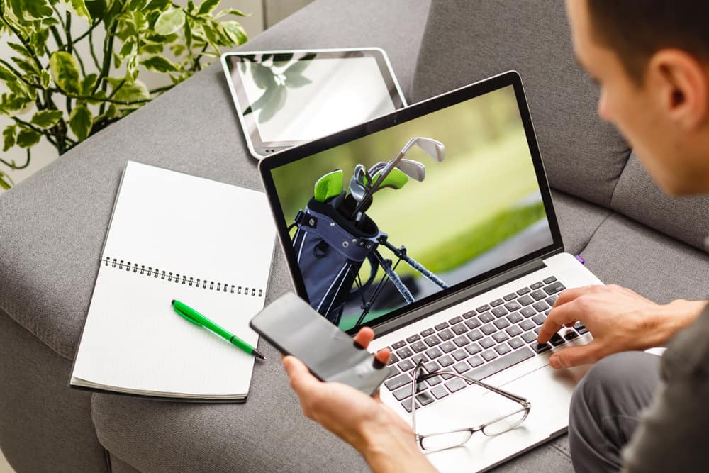 man holding mobile phone while typing on laptop at desk