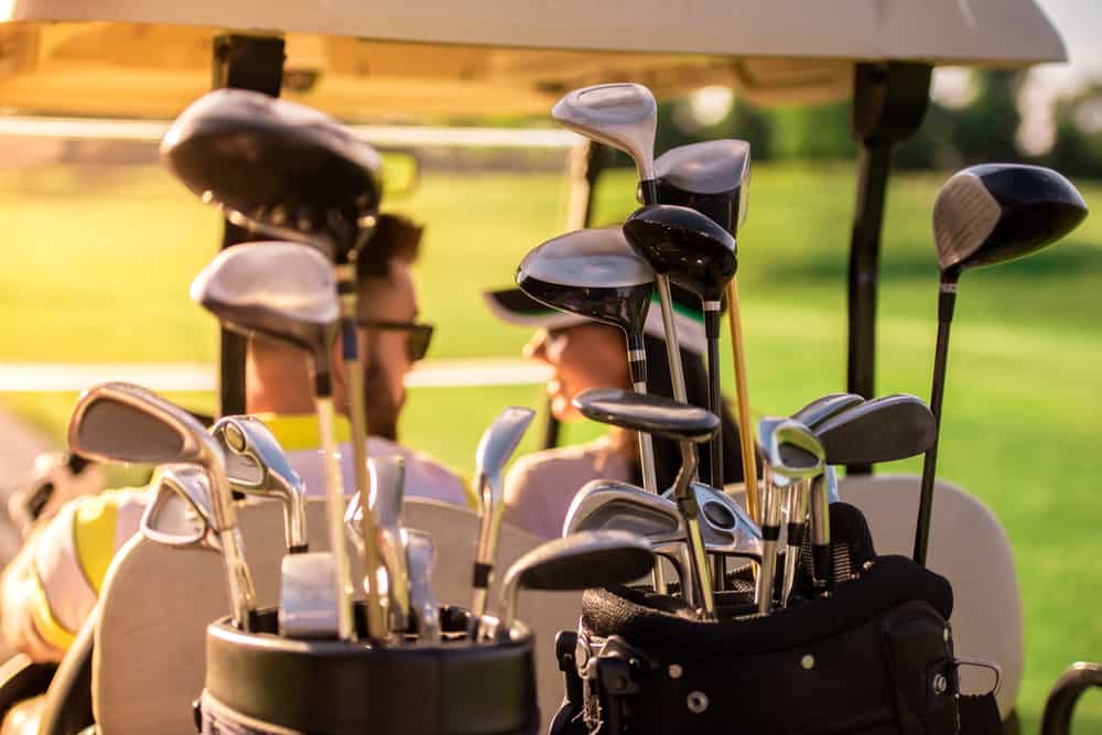 Back view of beautiful couple talking while driving a golf cart, golf clubs in the foreground