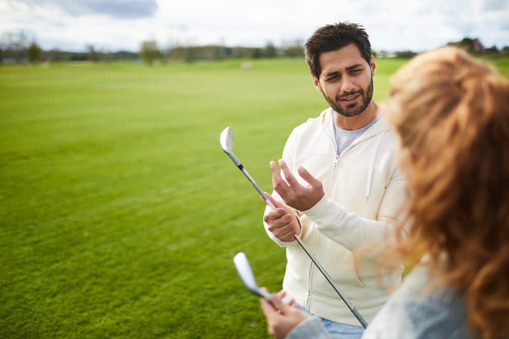 Active young man in casualwear having talk to his girlfriend while going to play golf on the field