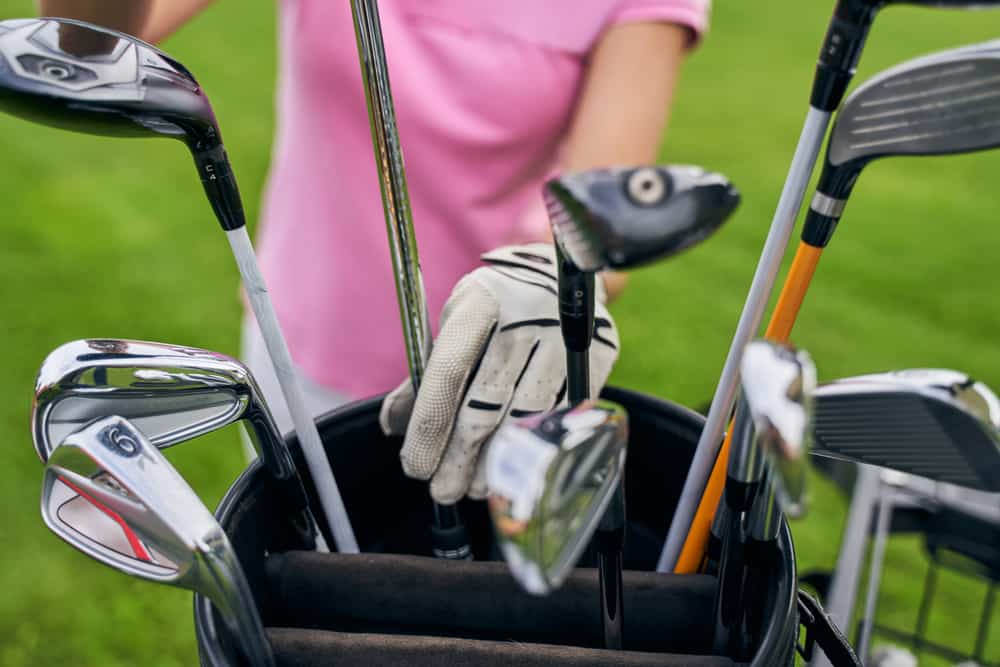 Cropped photo of a Caucasian sportswoman reaching for an iron club in a leather bag