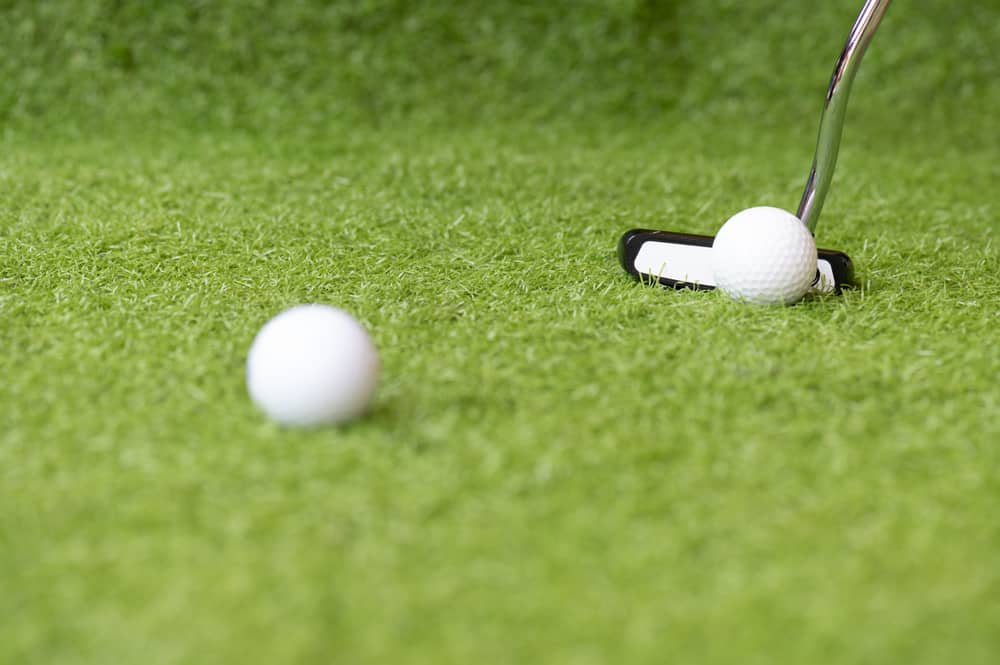 Golf club and golf ball on green grass background