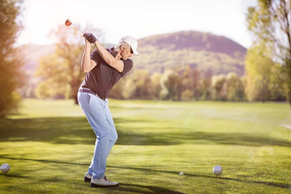 Senior golf player teeing off with golf club at sunset