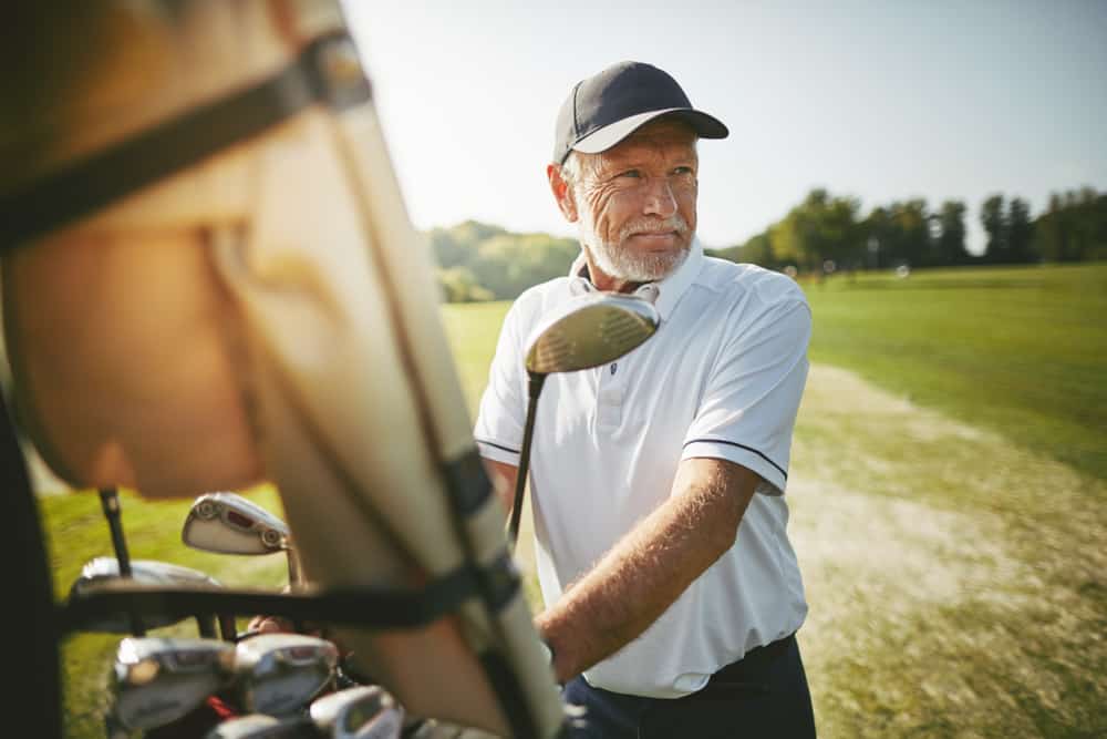 Smiling senior man standing by a golf cart