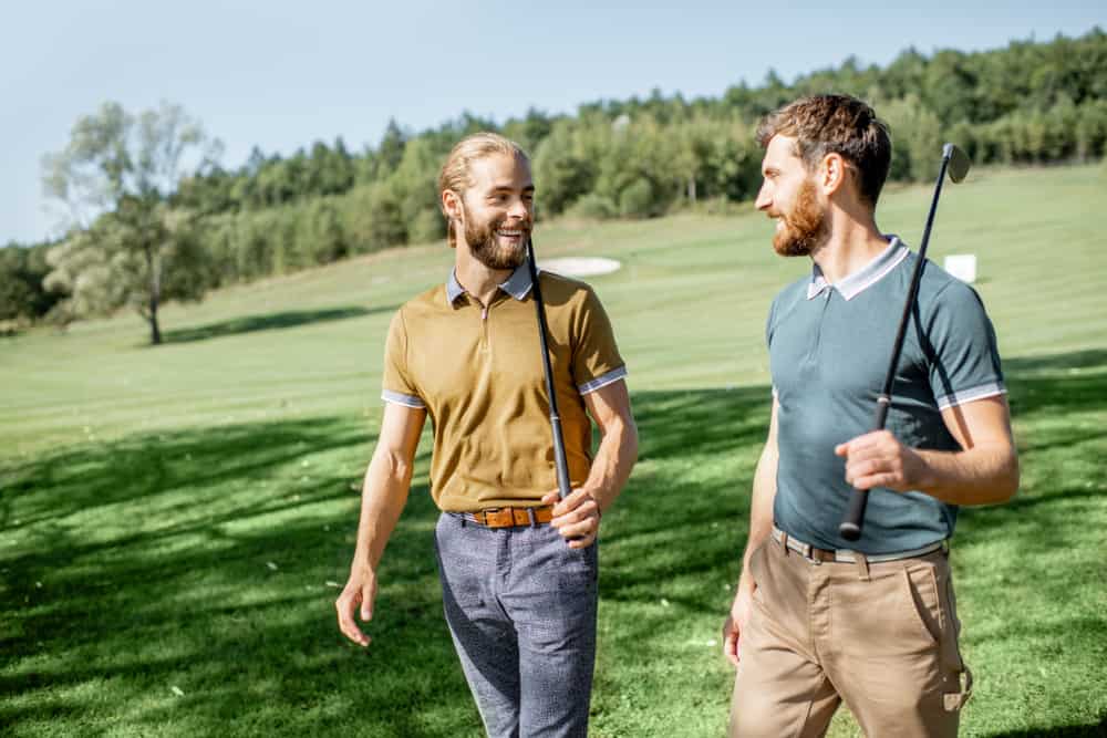 Two male best friends walking with golf equipment