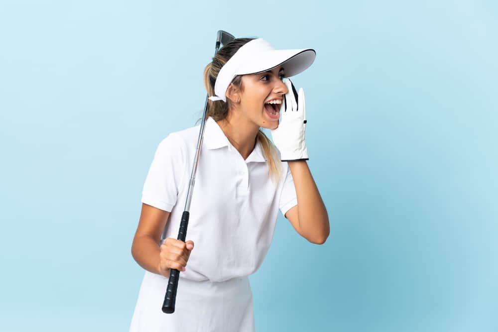 Young hispanic golfer woman over isolated blue wall shouting with mouth wide open to the side