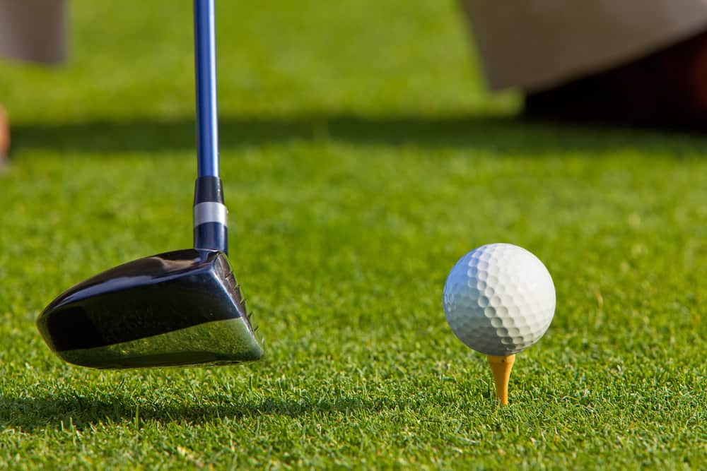 golf ball on a tee with the driver positioned ready to hit the ball