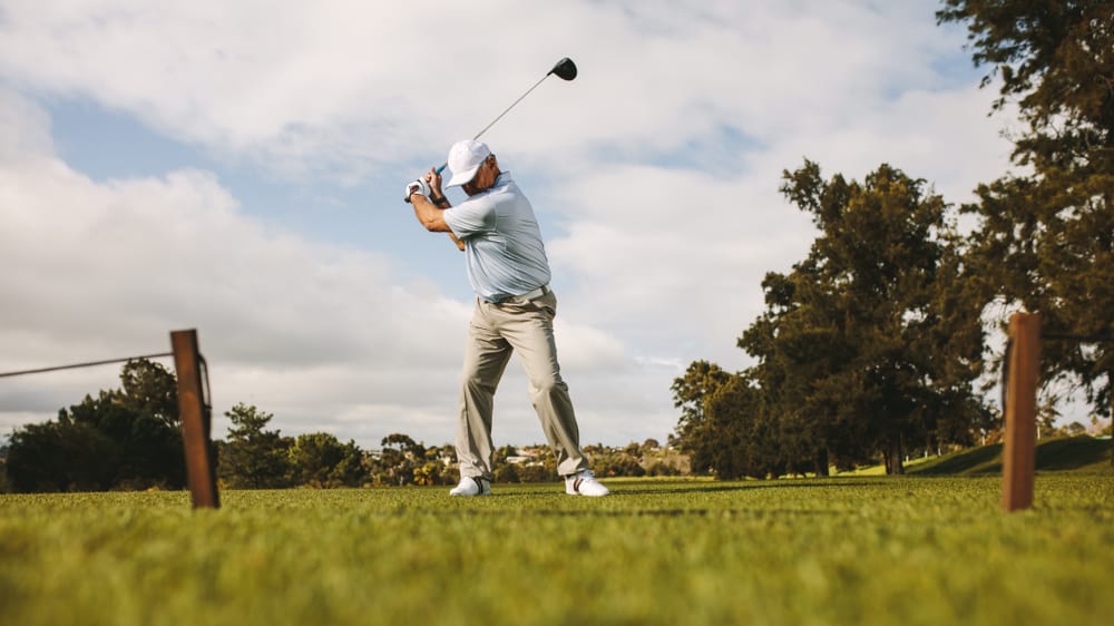 senior male golfer taking shot while standing on field