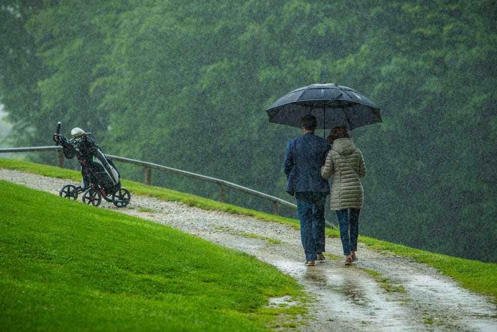 A couple with an umbrella in rain on a golf field