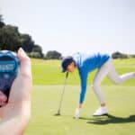Composite image of a woman holding a chronometer to measure performance against female golfer picking up golf ball