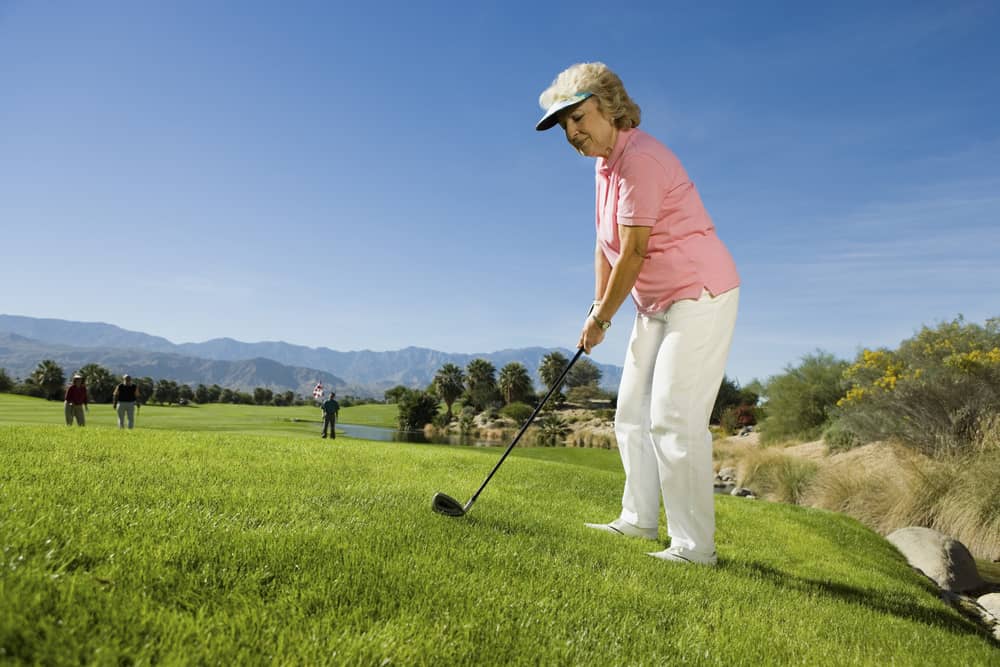 Full length of a senior woman playing golf with people in the background