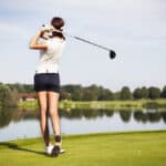 Girl golf player with driver teeing-off from tee-box