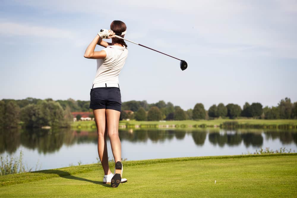 Girl golf player with driver teeing-off from tee-box