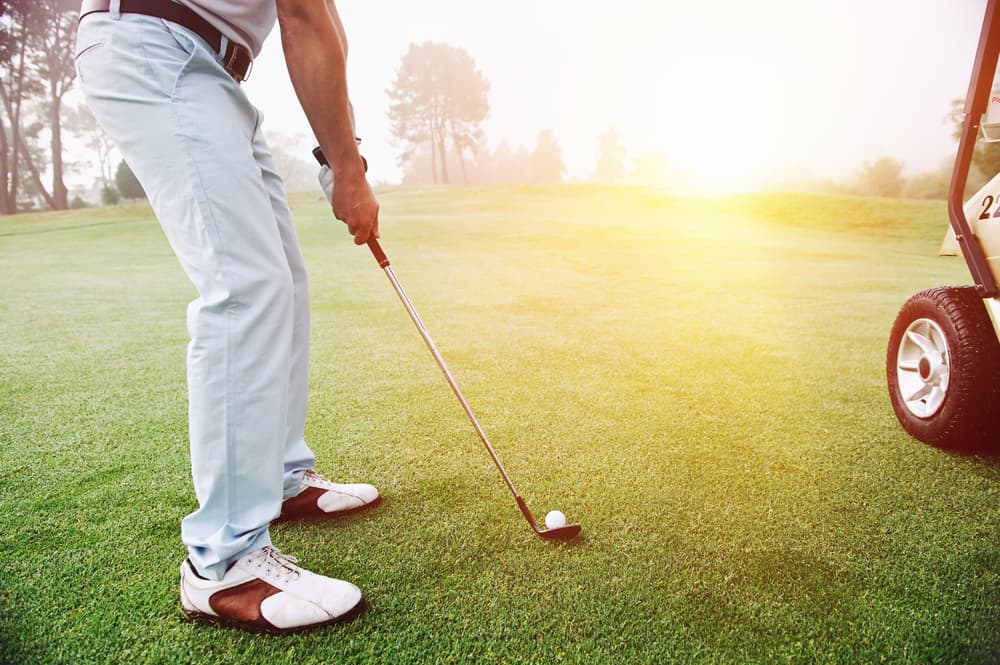 Golf approach shot with iron from fairway at sunrise