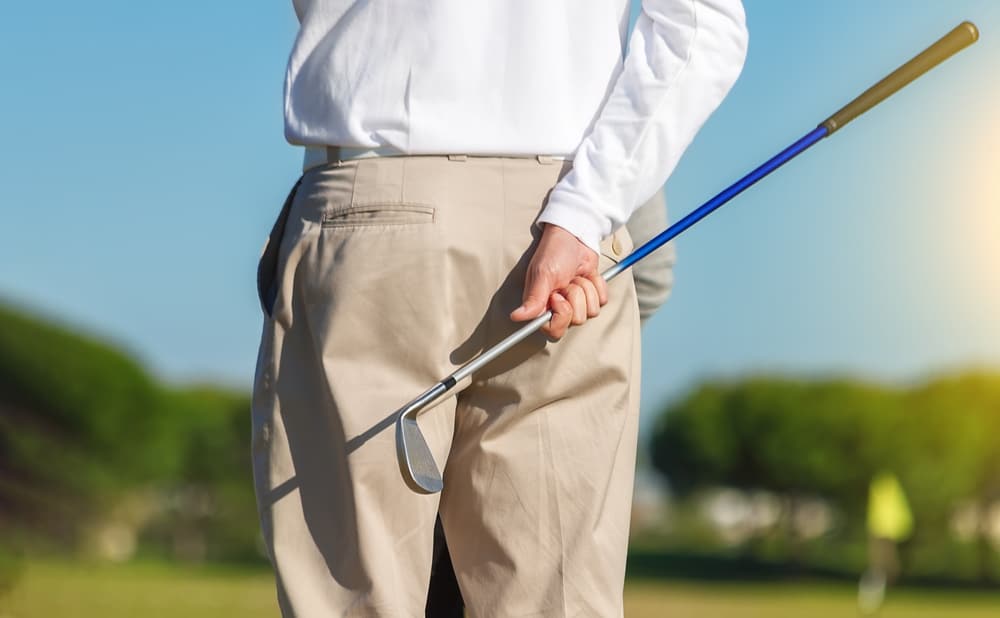 On focus shot of back of a golfer holding a club on a green golf field