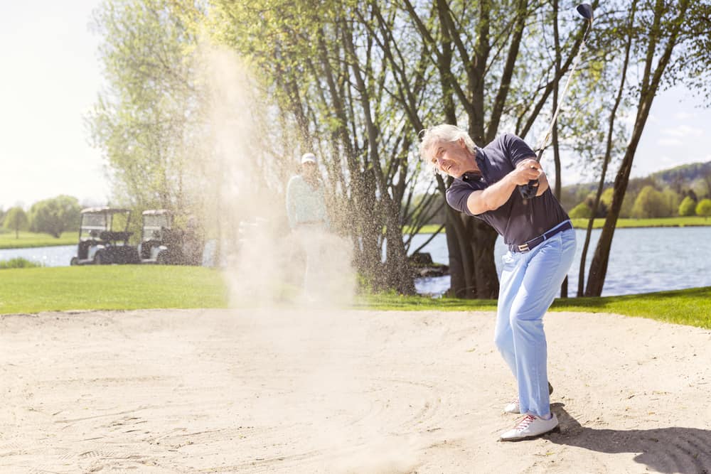 Senior golfer swinging golf club in sand bunker