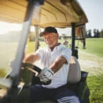 Smiling senior man driving a golf cart along a fairway