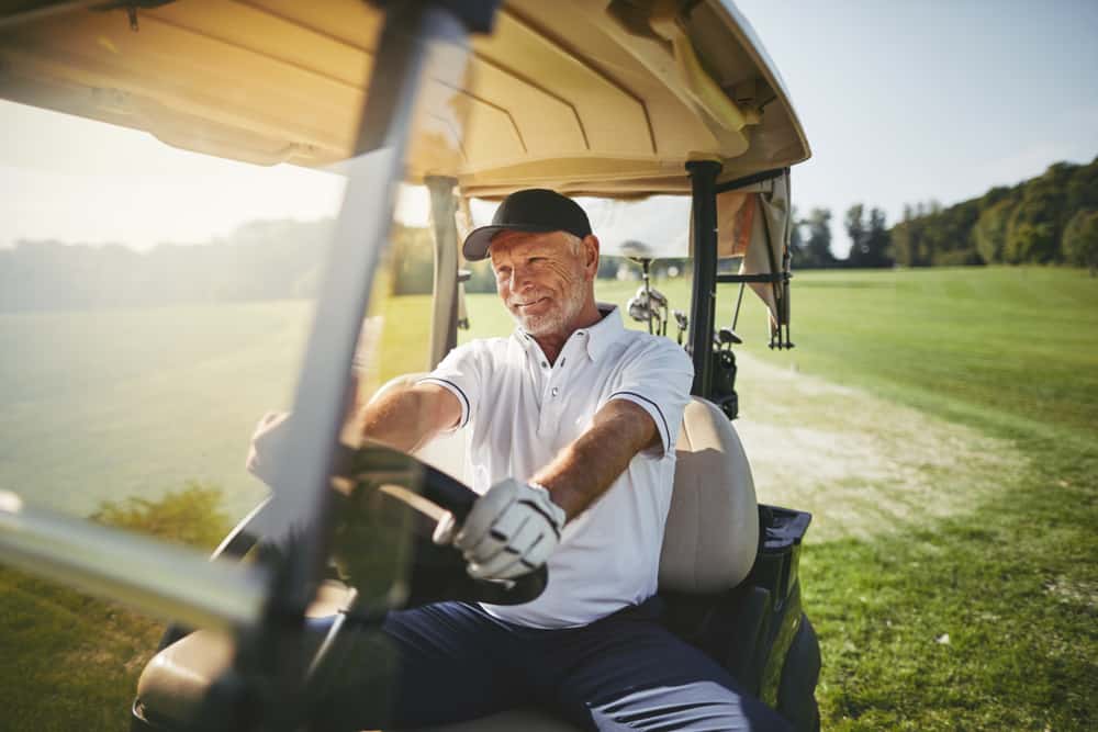 Smiling senior man driving a golf cart along a fairway