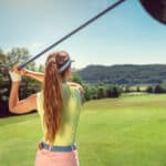 Woman with driver on golf course at the tee looking after a long ball