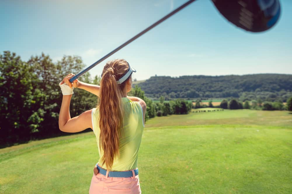 Woman with driver on golf course at the tee looking after a long ball