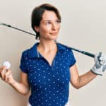 Young brunette woman with short hair holding ball and golf club smiling