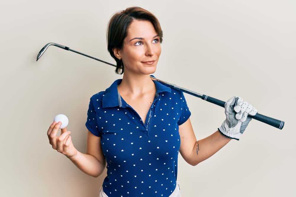 Young brunette woman with short hair holding ball and golf club smiling