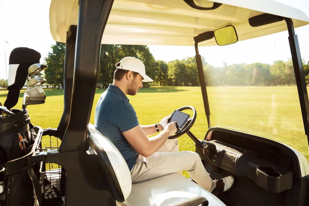 Young man sitting in a golf cart with a tablet computer