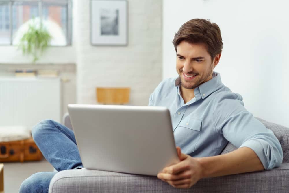 Young man smiling as he reads the screen of a laptop