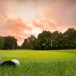 chipping a golf ball onto the green with golf club at sunset