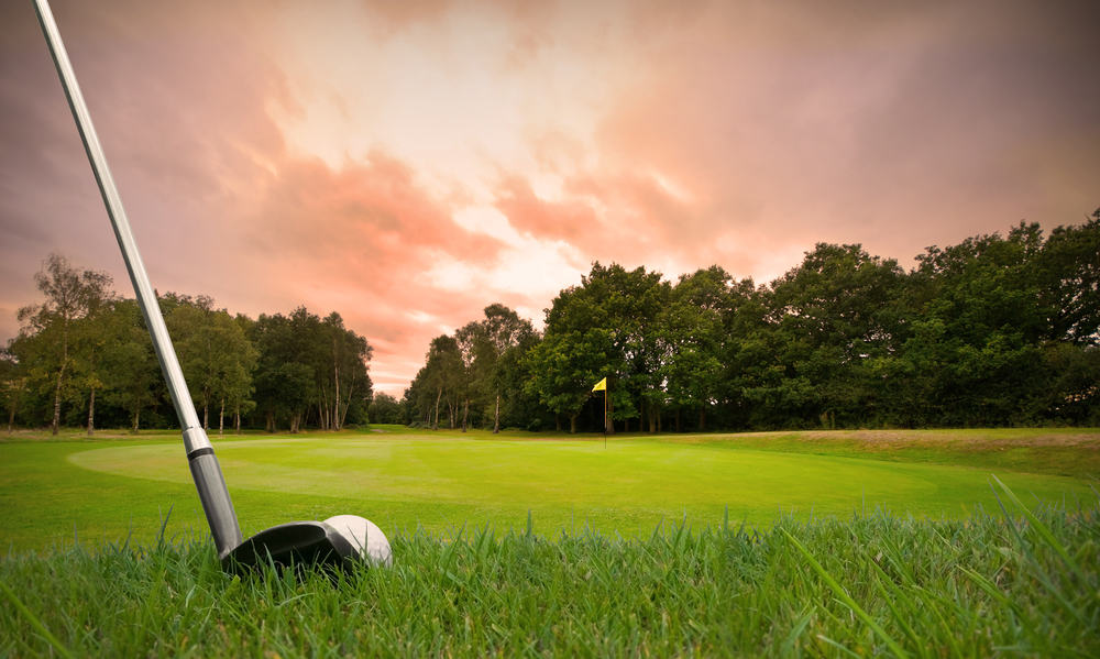 chipping a golf ball onto the green with golf club at sunset