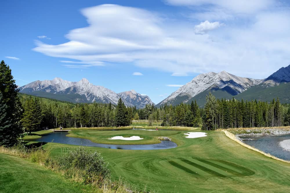 golf course surrounded by forest and big mountains in the background, on a beautiful sunny day in Kananaskis, Alberta, Canada