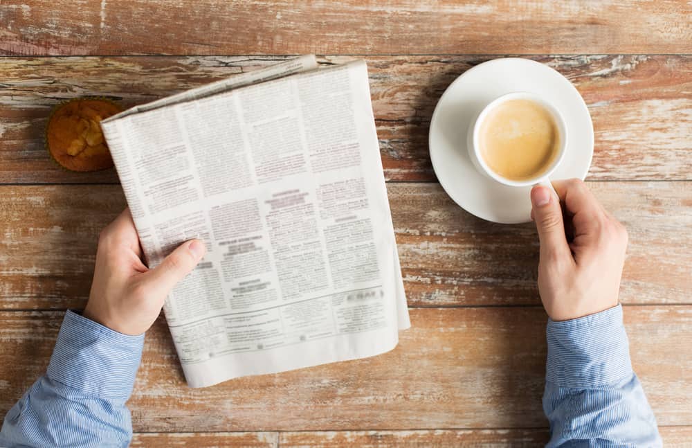 male hands with newspaper, muffin and coffee cup on table