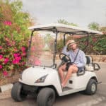 man straightens his hat while sitting in a white golf cart