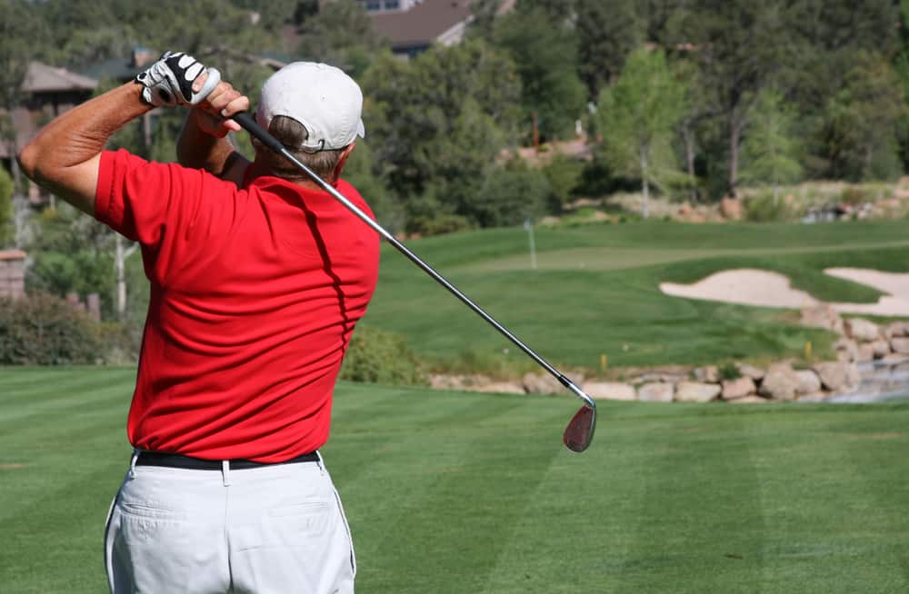 Male golfer with red shirt successfully hitting ball on green