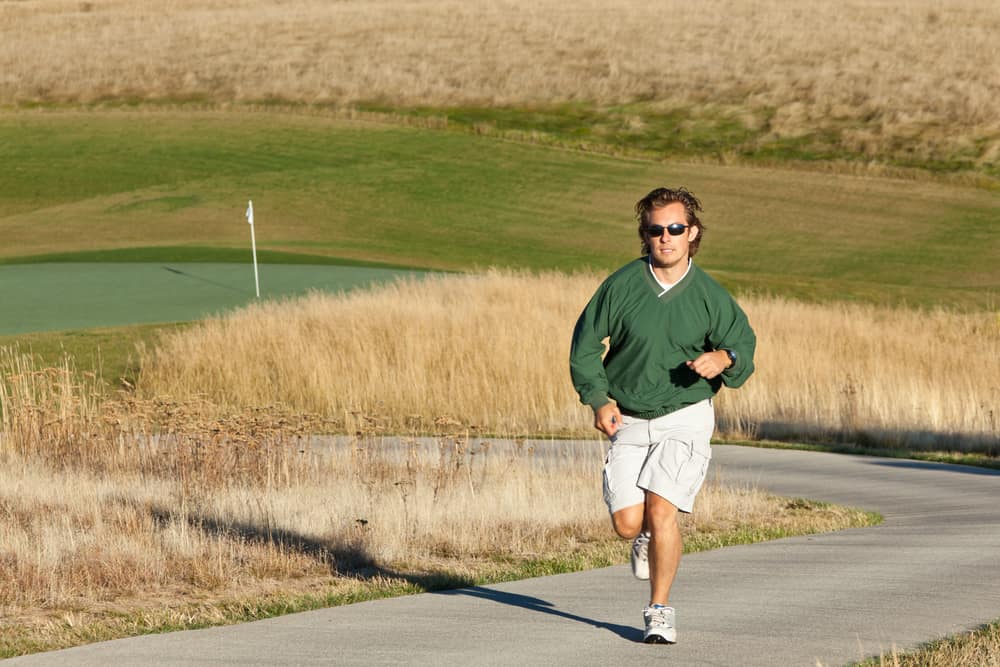 A man jogging on a paved pathway up a hill at an empty golf