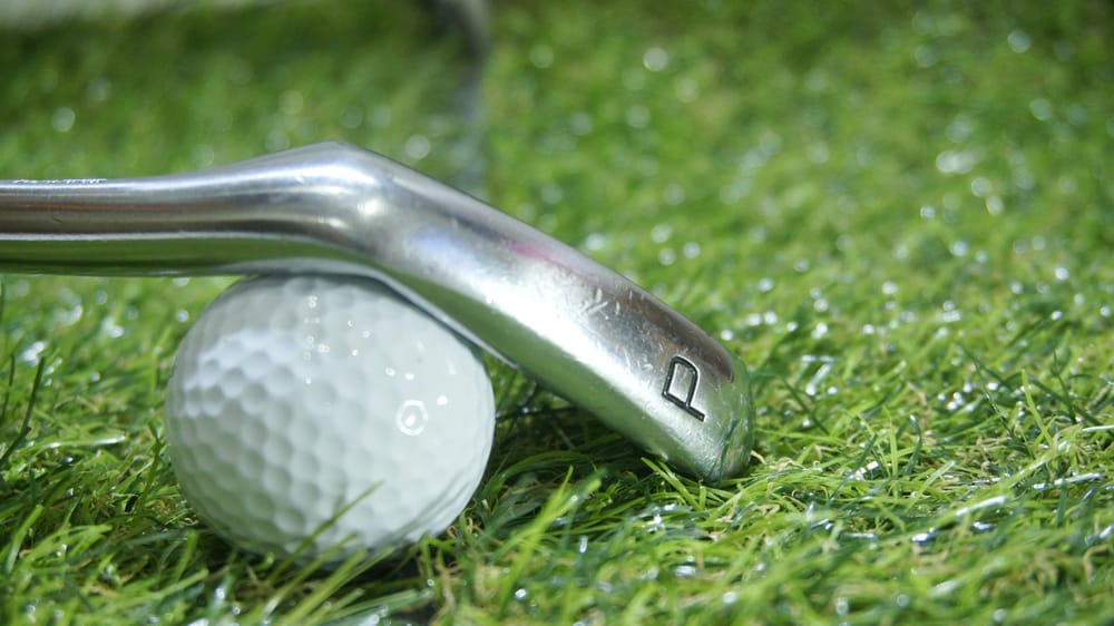 Golf iron and ball on green grass- iron P or Pitching wedge