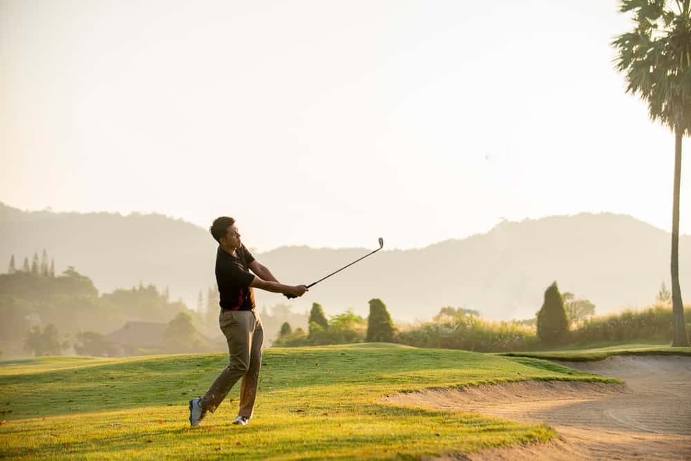 Golfer hitting golf ball on green