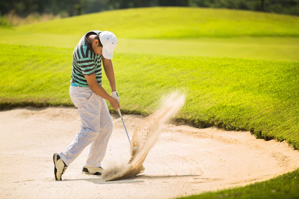 Golfers hit the ball in the sand