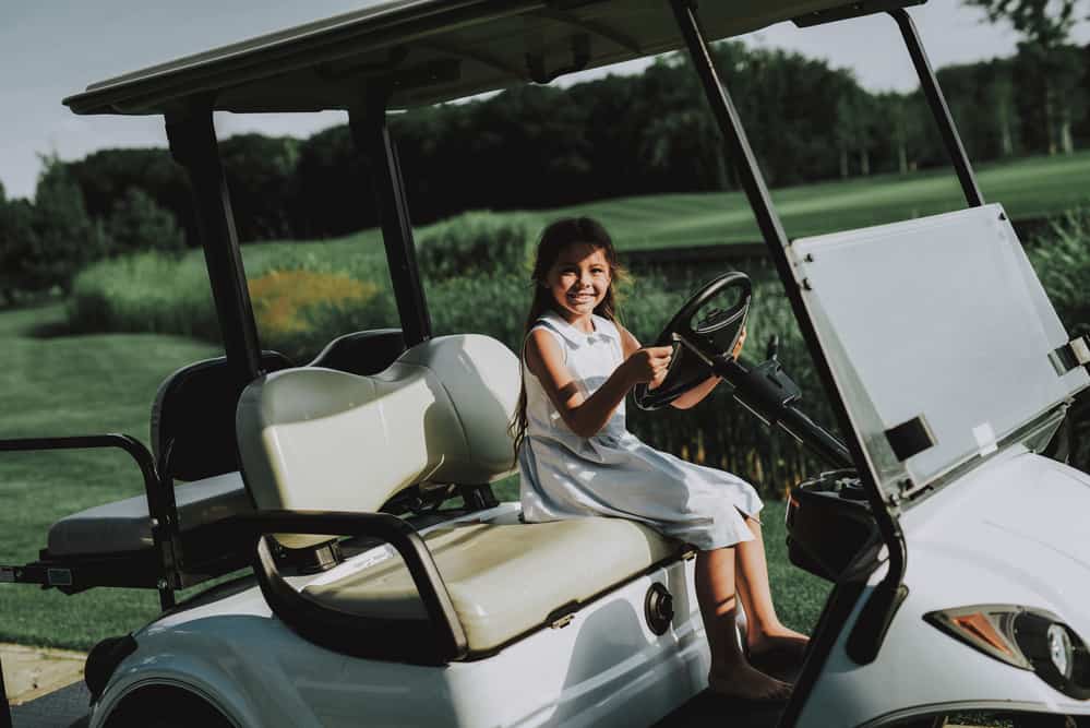 Little Girl in White Dress in Cart on Golf Field