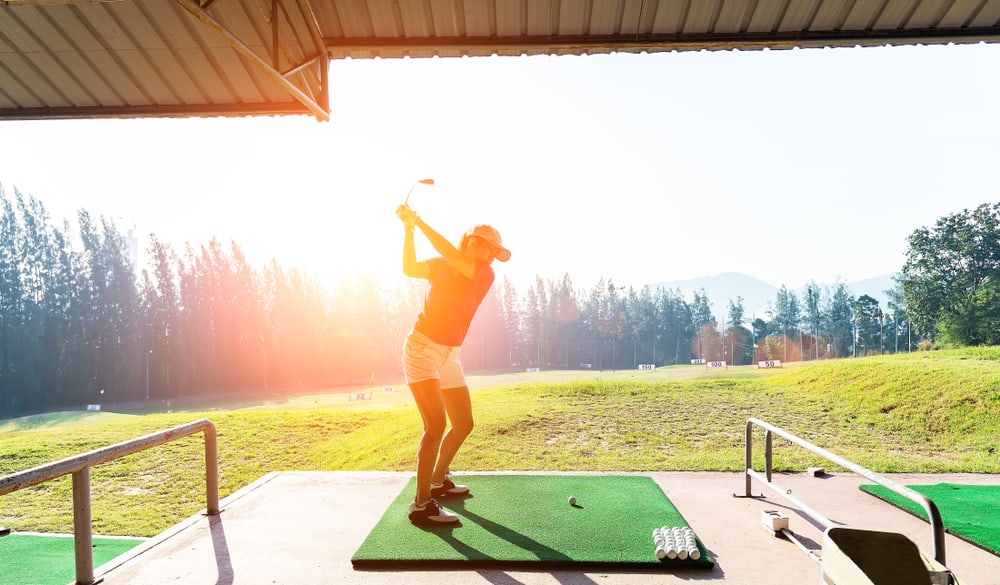 Young woman practices her golf swing on driving range