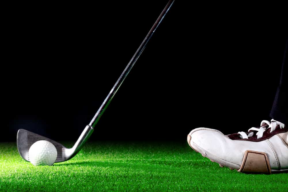 man ready to hit golf ball with golf iron on black background