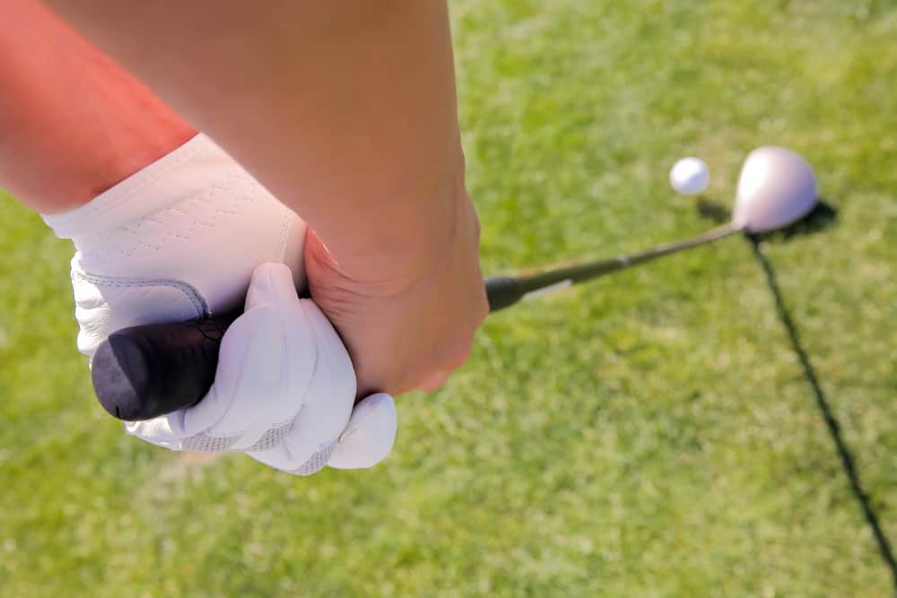 Close up shot of female hands in glove with a golf driver club and ball on green fairway grass