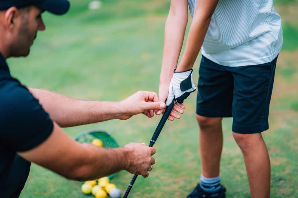 Golf Instructor adjusting young boy’s grip