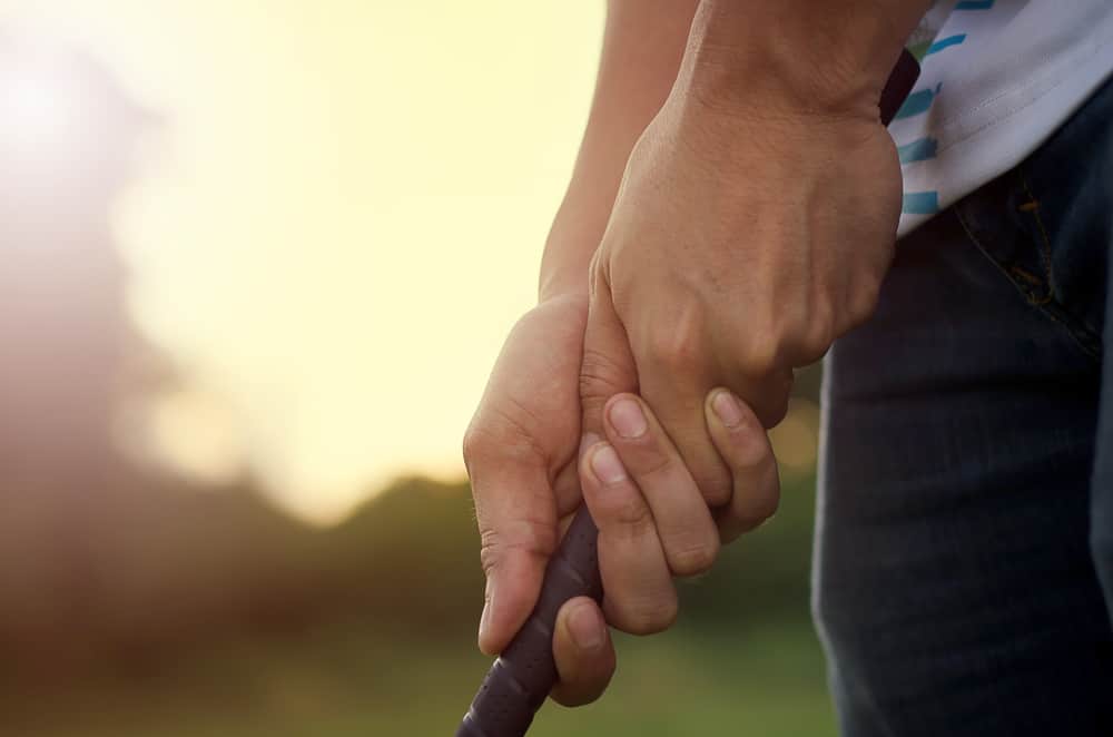 Man's hand holding a golf club with a warm light at sunset