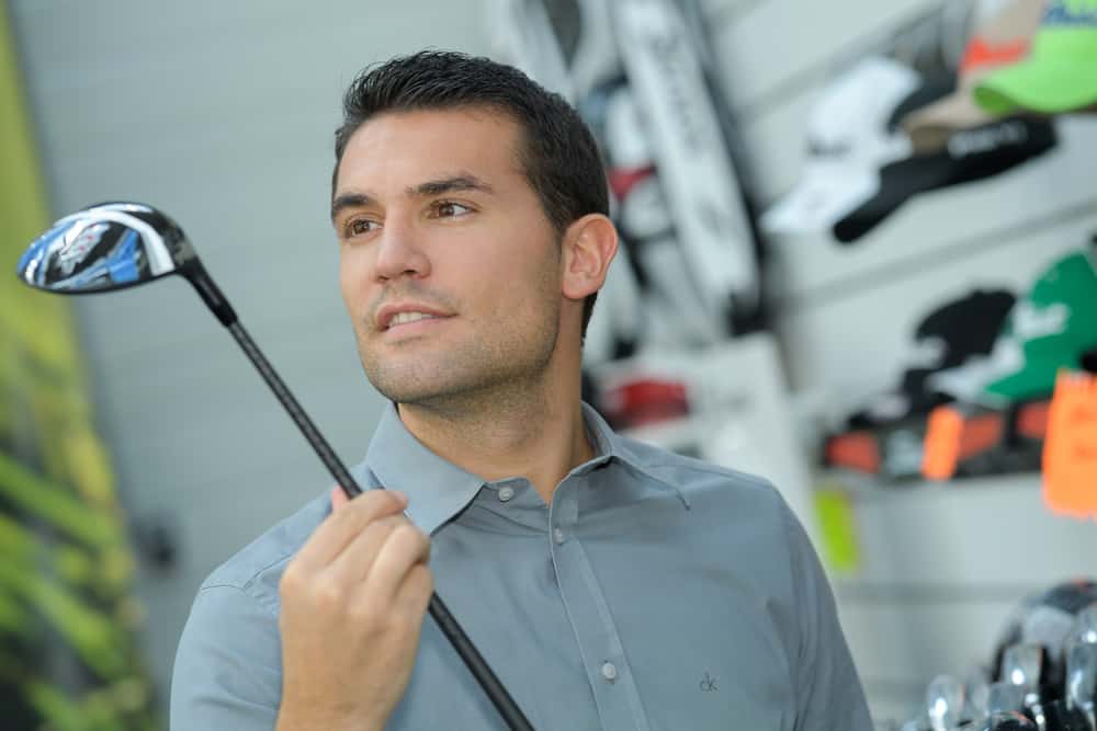 Person holding with hand golf club in a golf shop