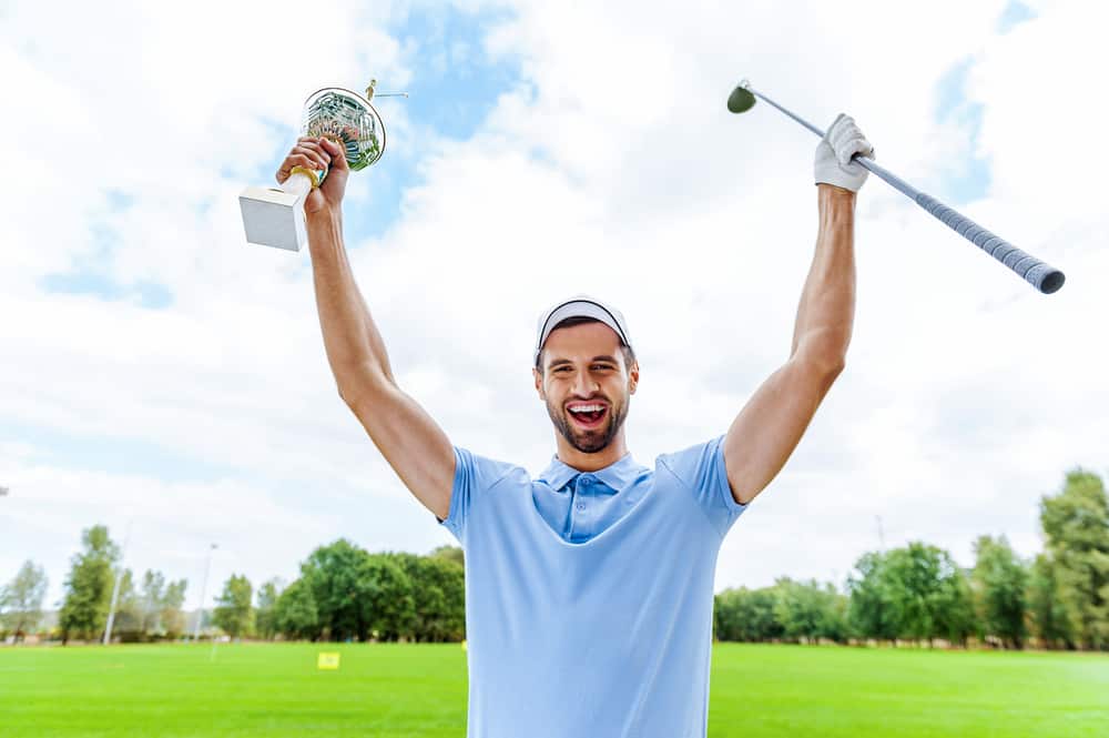 Happy male golfer holding trophy and driver