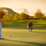 Two male golf player at sunset on green, one putting , with beautiful fairway in background
