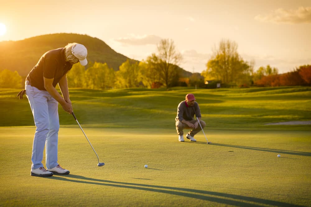 Two male golf player at sunset on green, one putting , with beautiful fairway in background